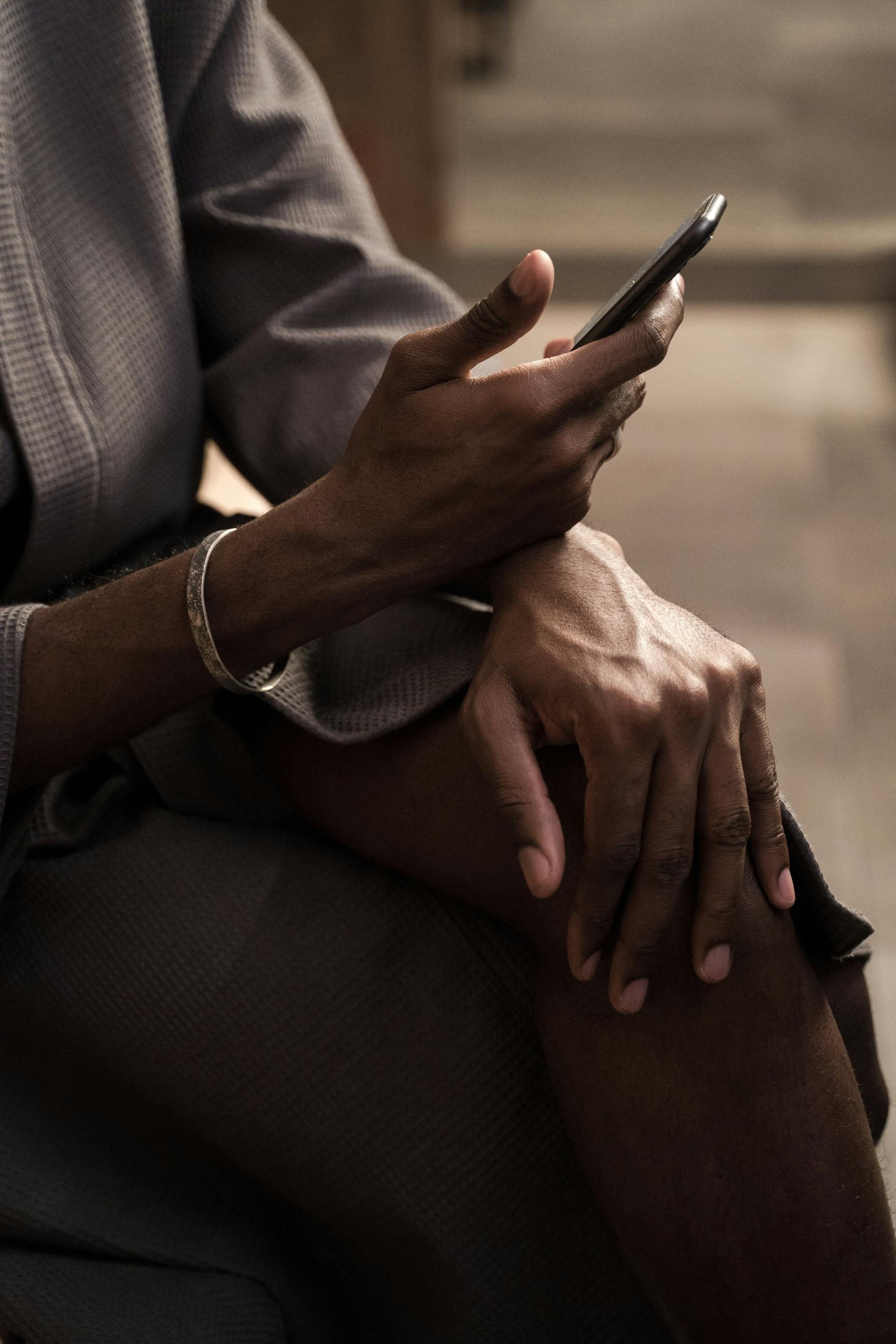 A close-up photo of a person using a smartphone, focusing on their hands in a cozy indoor setting.